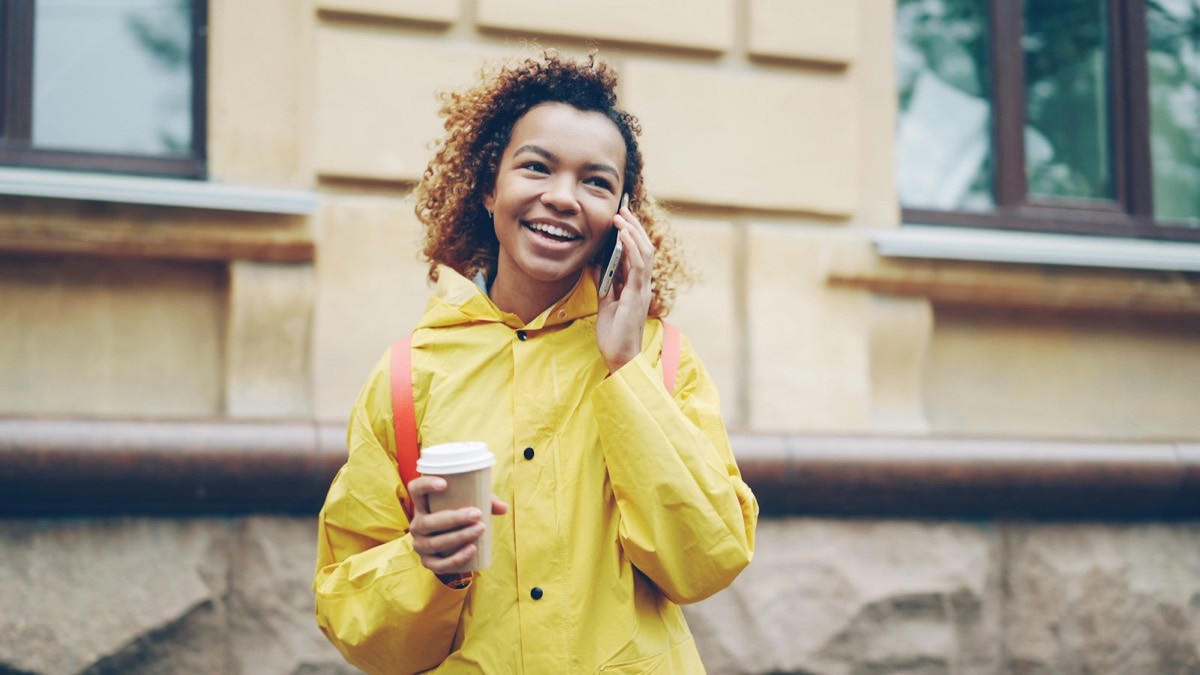 A woman in a yellow raincoat laughing on her phone on a city street