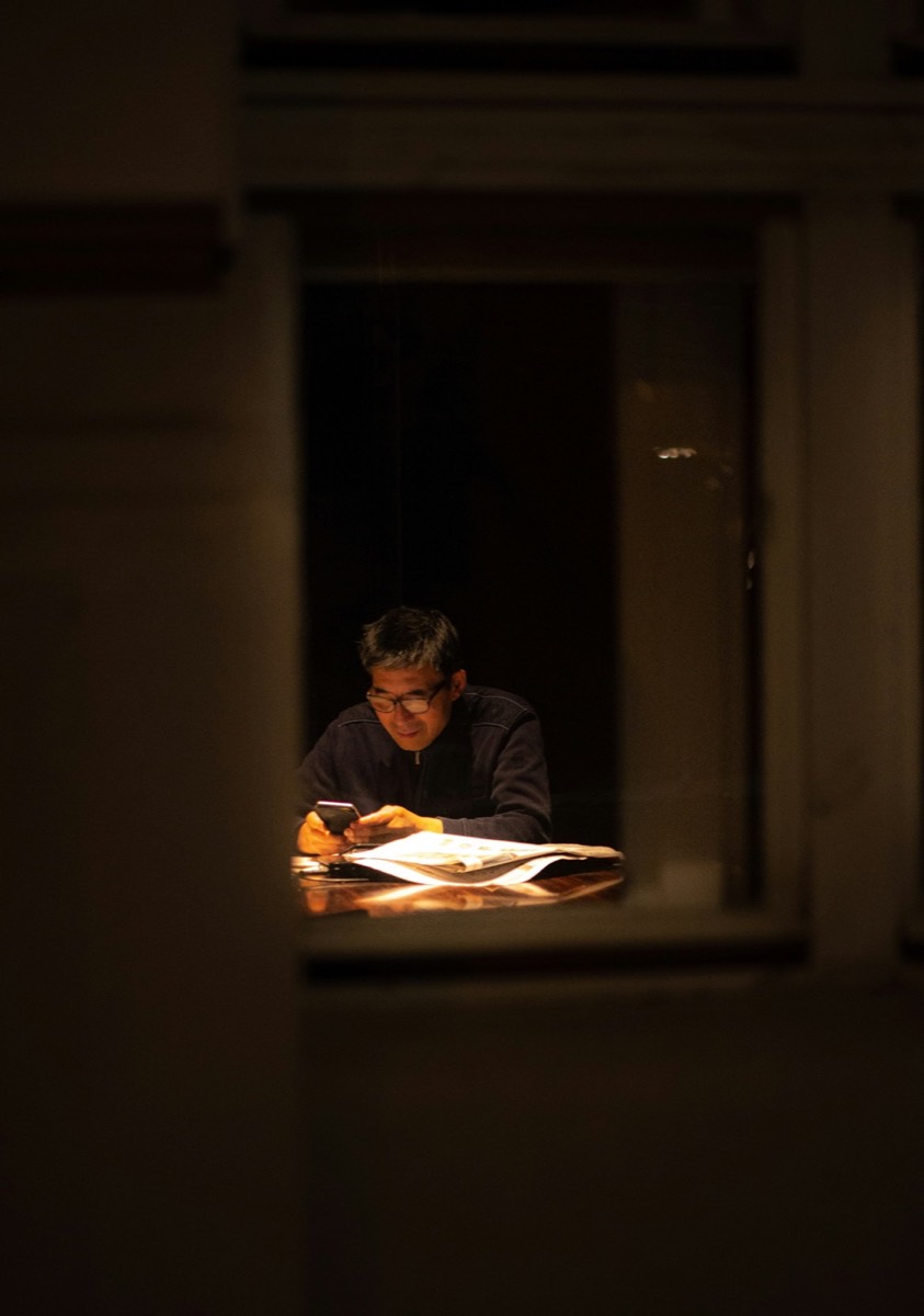 A man reading by lamplight at a window late at night